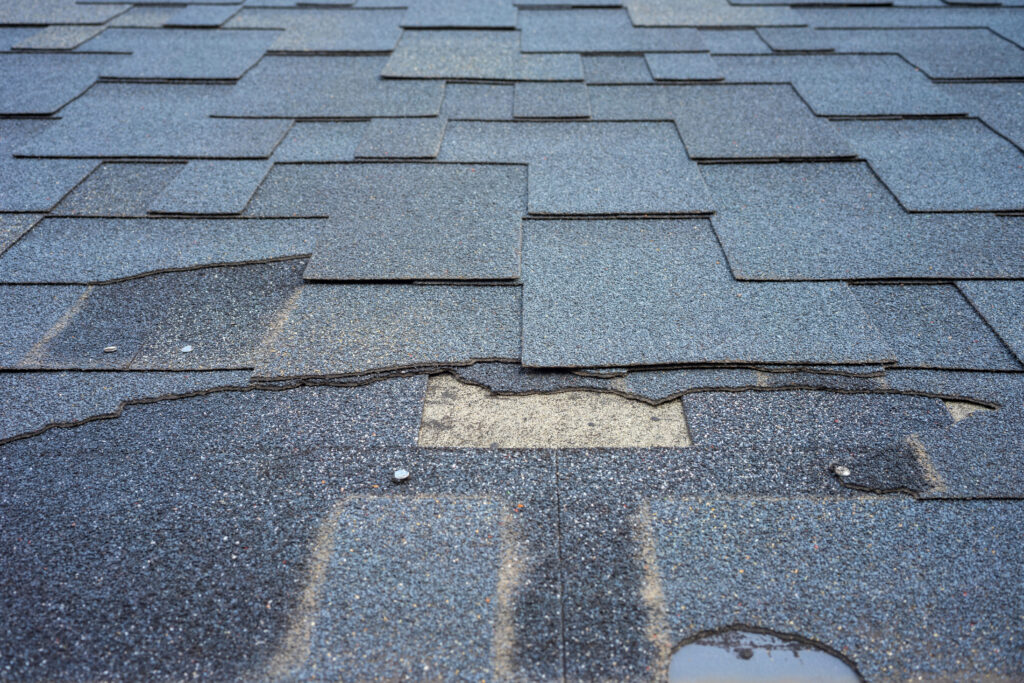 Сlose up view of bitumen shingles roof damage that needs repair.